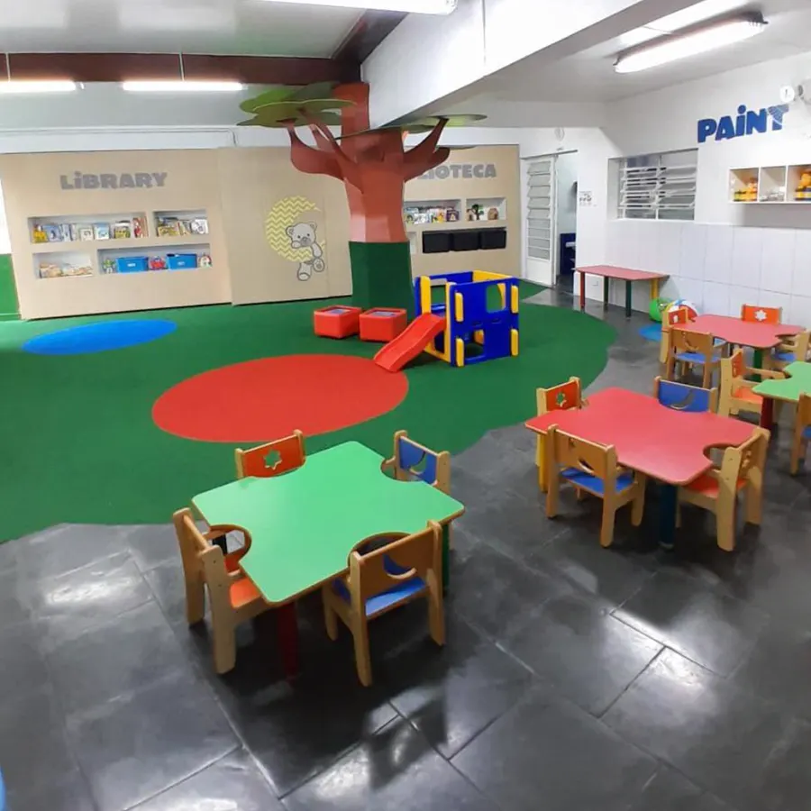 Espaço com biblioteca, árvore decorativa e mesas coloridas